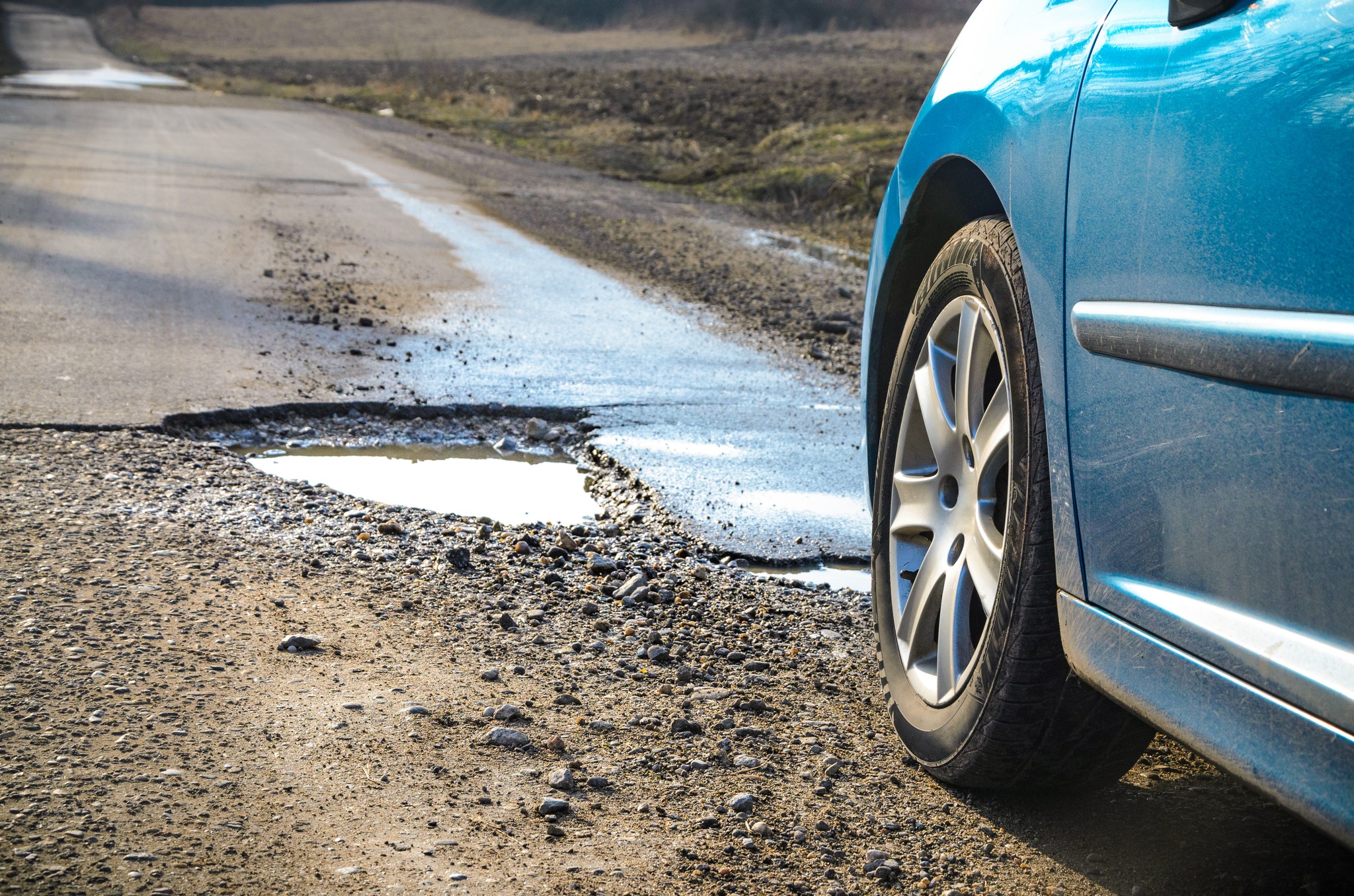 Blue car stop behind rain filled pot hole.