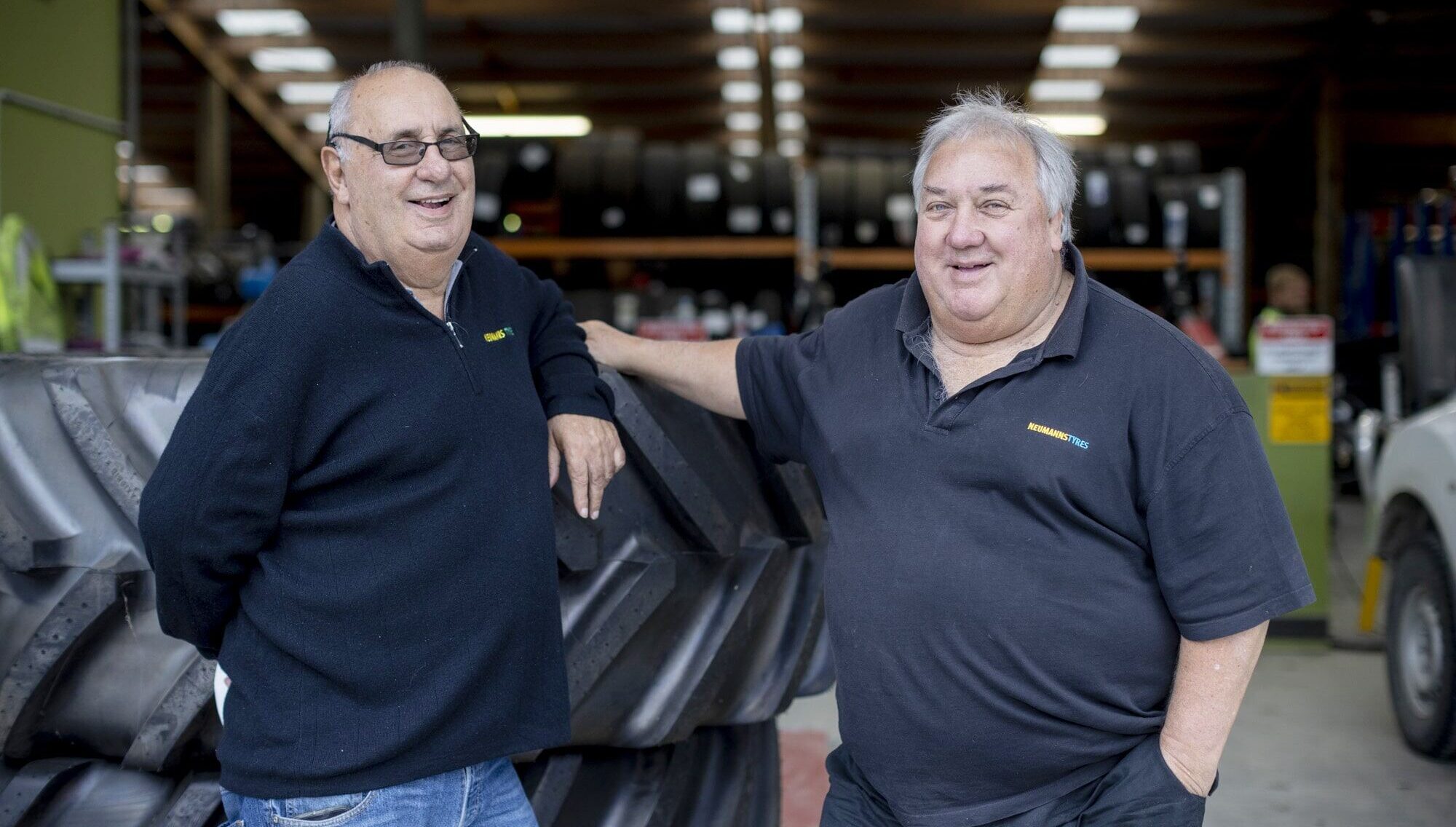 Owners of Neumanns Tyres, Alan & Ian lean against stack of tyres.