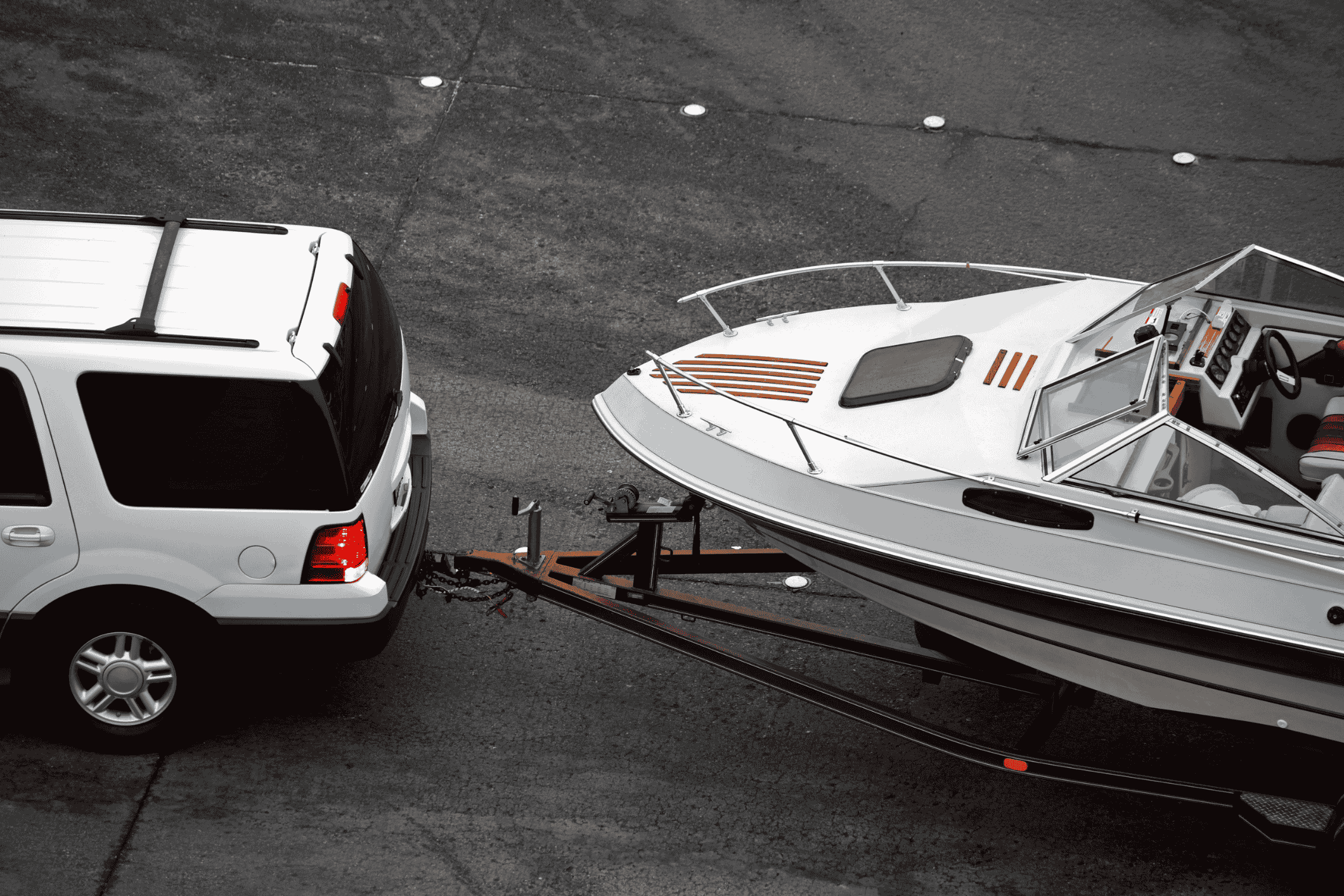 White SUV pulling white speed boat on trailer from above